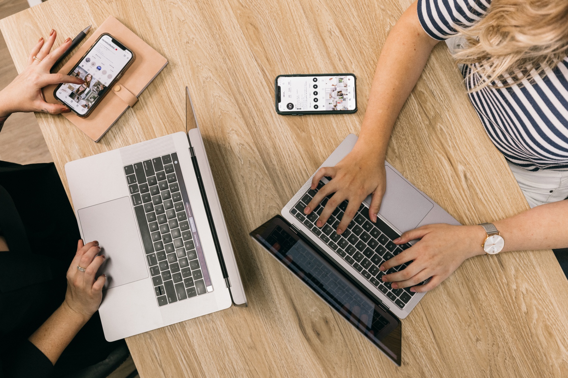 Two colleagues working together across laptops and phones at a shared desk